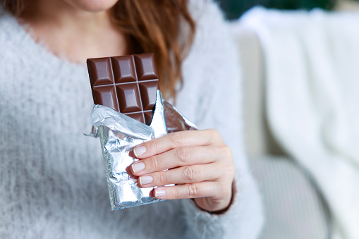 Hands of a woman holding a tile of chocolate. Chocolate bar in silver foil in woman's hand