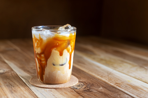 a glass of ice caramel macchiato coffee on  wooden table, summer beverages.
