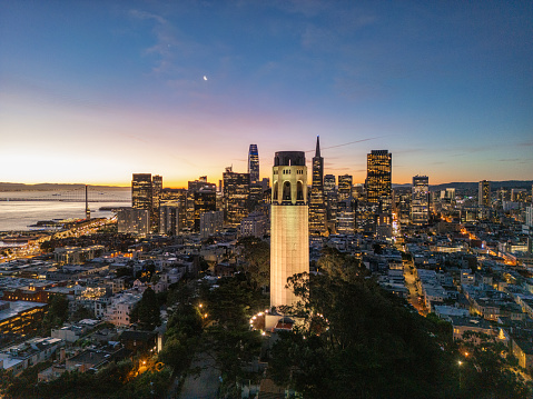 An aerial view of the San Francisco skyline with Coit Tower in the foreground at sunrise.