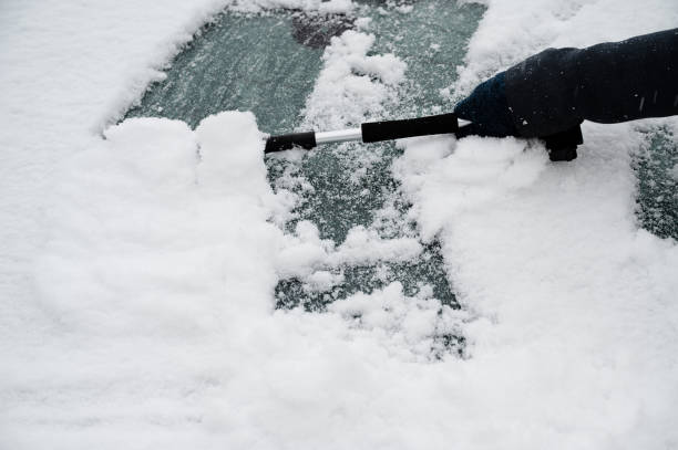 driver is removing snow from car windshield with ice scraper and broom, clean car window from icy frost, winter season - snow car window ice scraper foto e immagini stock