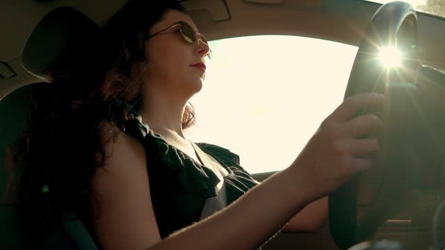 Woman in sunglasses driving car with hands on steering wheel to control vehicle at sunset