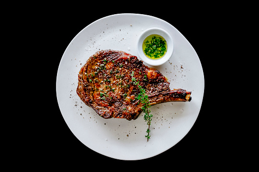 Cooked rib-eye on a white plate and black background.