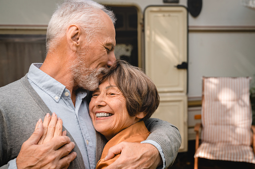 Portrait of happy smiling senior old couple grandparents hugging bonding embracing kissing during travel trip voyage by trailer camper van motor home