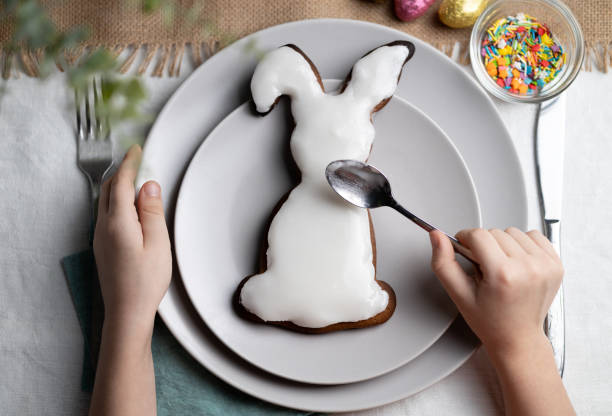 Top view of bunny shaped gingerbread cookie. Hands of child decorating biscuit with icing on Easter holidays