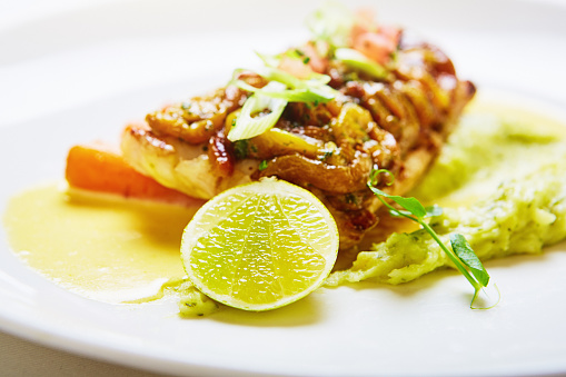 Healthy dish of fish and vegetables served with a halved lime on a white plate.