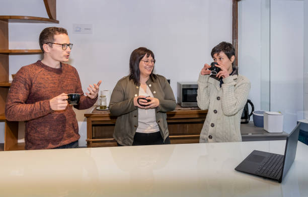 istock Three co-workers having a conversation while they consult a laptop and have coffee on a break from work in office. Workaholics concept 1935367249