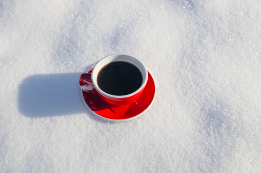 Red ceramic cup of espresso coffee stand on the snow on snow background of a winter landscape. A walk in the fresh air.