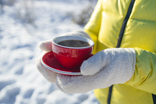 Woman in woolen gloves holds a red cup of coffee in the winter city outdoors. Hot and warming drinks in the winter concept. Hands close up. High quality photo