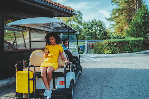 Beautiful mixed race woman sitting at the back of golf cart, just arriving in tourist resort