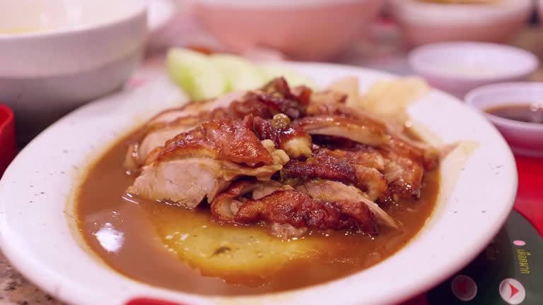 Dipping a slice of Peking duck in a spicy sauce that is served in a platter at a restaurant in Bangkok, Thailand.