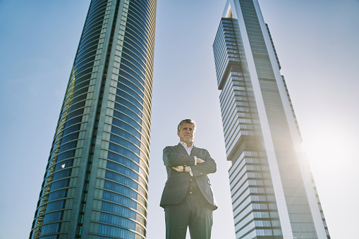 mature businessman with arms crossed and an office building in the background