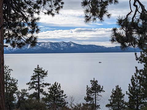 Looking onto a lake from a hill with snow covered mountains in the distance and a small boat crossing the lake.