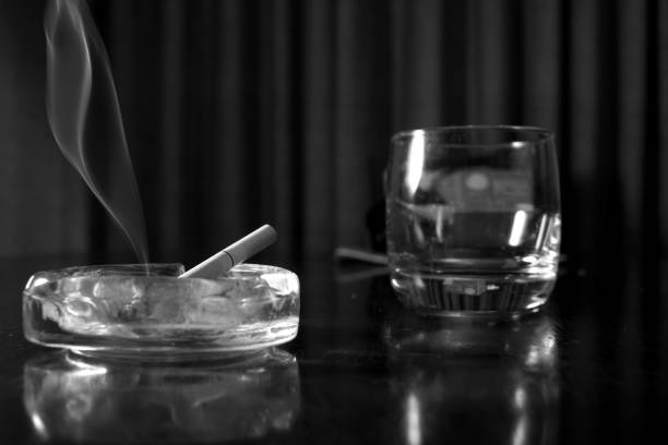 istock ashtray with a lit cigarette next to an empty glass on a table, black and white photograph, mysterious and melancholic atmosphere. 1935455458
