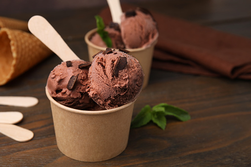 Paper cups with tasty chocolate ice cream on wooden table, closeup. Space for text