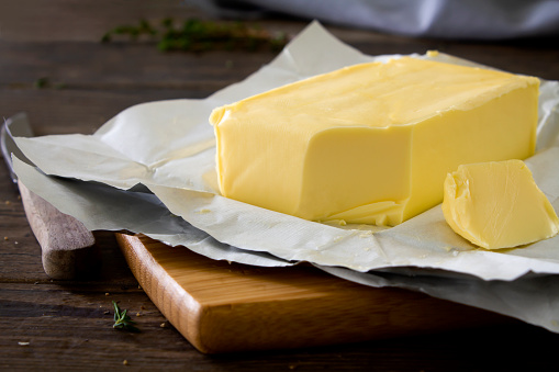 Close up shot of a block of butter on a chopping board, cut with a knife on a rustic wooden kitchen table.