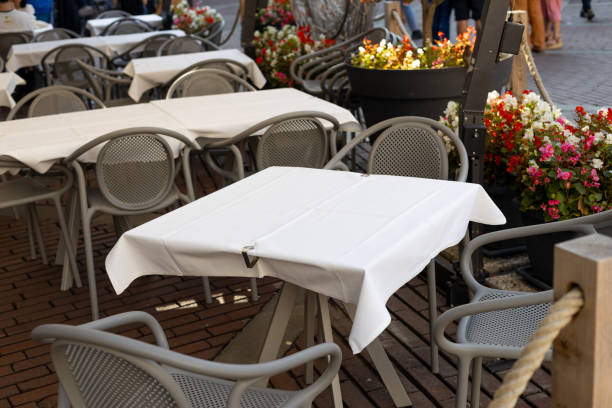 istock Dining outdoors. Outdoor street cafe tables ready for service. Empty cafe terrace with table and chair. Table of outdoor cafe on sidewalk with colorful plants and flowers 1935466650