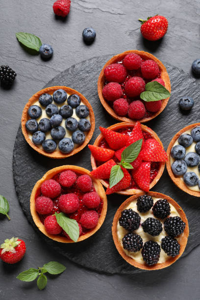 istock Tartlets with different fresh berries on black table, flat lay. Delicious dessert 1935466655