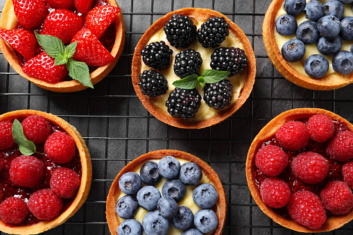 Tartlets with different fresh berries on grey table, flat lay. Delicious dessert