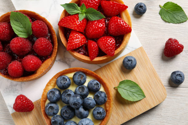 istock Tartlets with different fresh berries on light wooden table, flat lay. Delicious dessert 1935468222