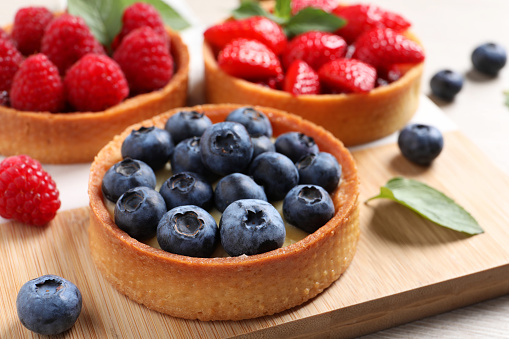Tartlets with different fresh berries on board, closeup. Delicious dessert