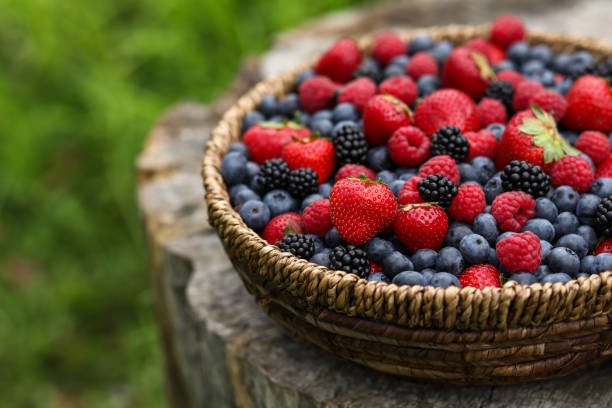 Wicker bowl with different fresh ripe berries on wooden surface outdoors, space for text