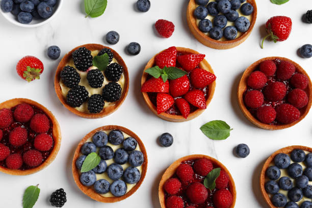 istock Tartlets with different fresh berries on white marble table, flat lay. Delicious dessert 1935469294