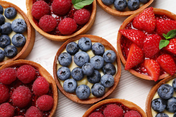 istock Tartlets with different fresh berries on white wooden table, flat lay. Delicious dessert 1935470338