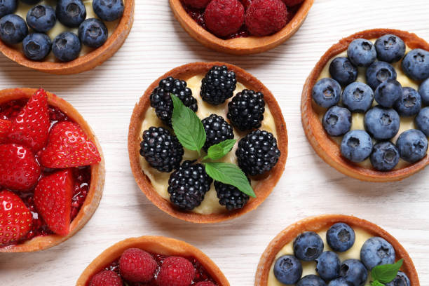 istock Tartlets with different fresh berries on white wooden table, flat lay. Delicious dessert 1935470866