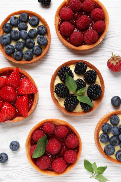 istock Tartlets with different fresh berries on white wooden table, flat lay. Delicious dessert 1935470875