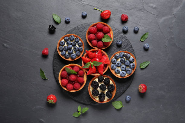 istock Tartlets with different fresh berries on black table, flat lay. Delicious dessert 1935471917