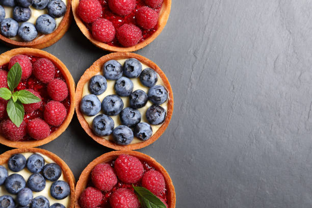 istock Tartlets with different fresh berries on black table, flat lay and space for text. Delicious dessert 1935472455