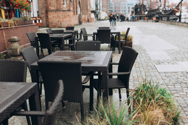 istock Dining outdoors. Outdoor street cafe tables ready for service. Empty cafe terrace with table and chair. Table of outdoor cafe on sidewalk with plants, rainy day 1935480955