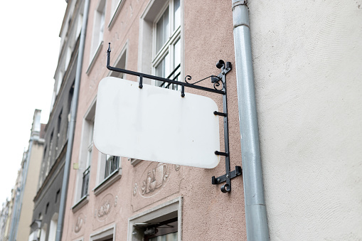 Mock up of a white blank empty vintage sign for cafe, restaurant name and logo, in an old town city.