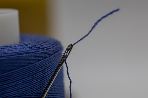 A closeup of a small needle in a blue thread on the blurry background