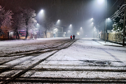 An empty winter night street with two human silhouettes at the end.