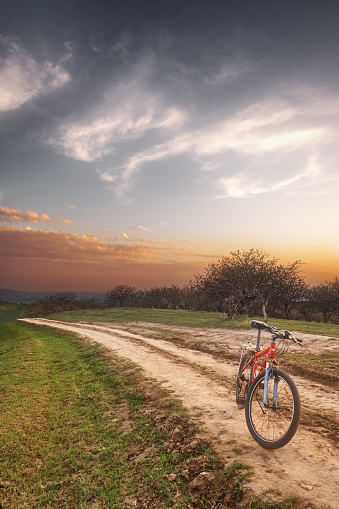 A bicycle is standing on a dirt road in the mountains against the backdrop of a beautiful evening sky, in a vertical frame