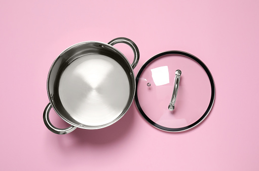 Steel pot and glass lid on pink background, flat lay