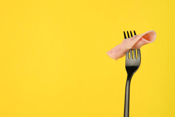 istock Fork with tasty slice of ham on yellow background, space for text 1935513510