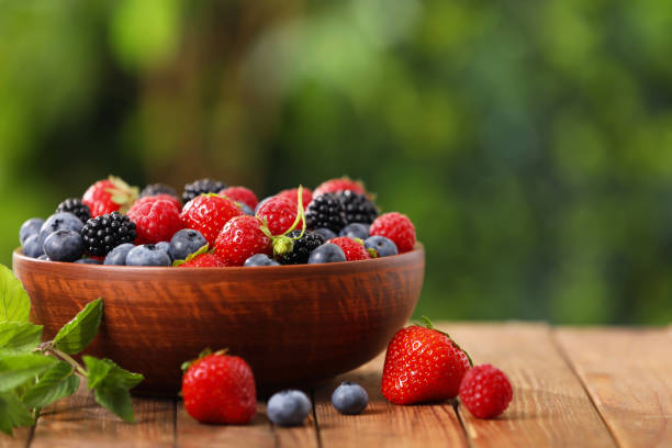 istock Bowl with different fresh ripe berries on wooden table outdoors, space for text 1935514068