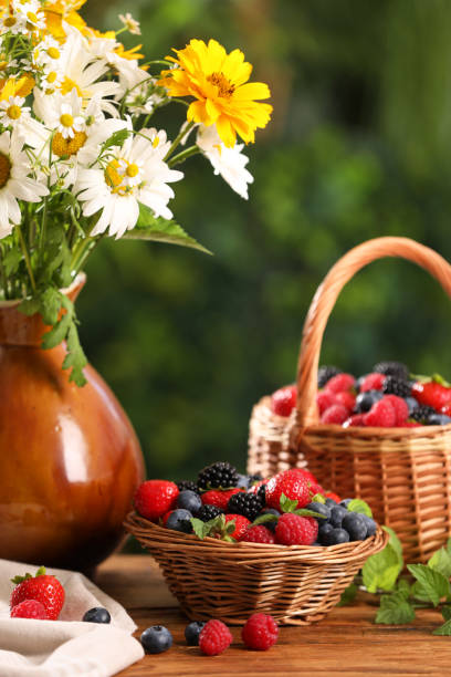 istock Different fresh ripe berries and beautiful flowers on wooden table outdoors 1935514607