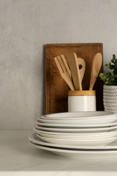 istock Set of clean plates and different kitchen utensils on light table near wall 1935515199