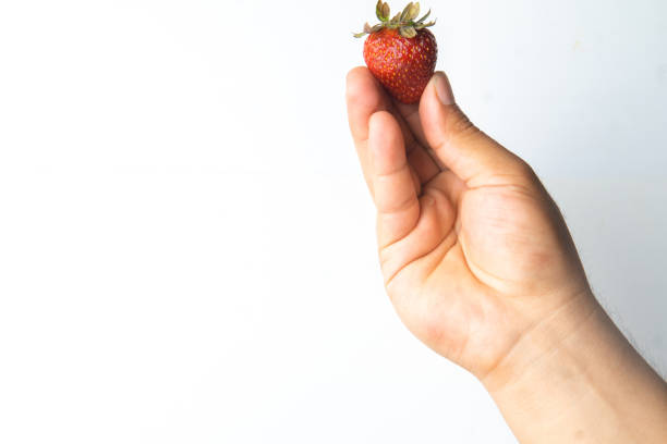 man's hand holding fresh organic strawberries on a neutral white background