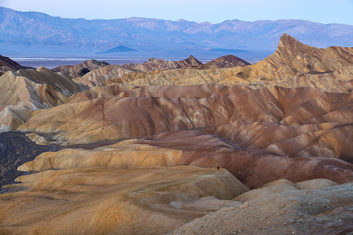 Embarking at sunrise on the Golden Canyon loop from Zabriskie Point in Death Valley National Park, alone woman becomes a mere dot against the grandeur landscape. Breathtaking moment capturing the enormity of nature's canvas