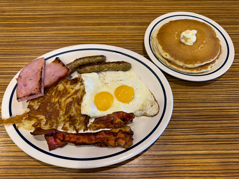 An American breakfast of fried eggs, bacon, ham, sausages and hash brown with pancakes and butter