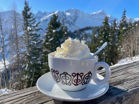 Apres ski, after ski in the Alps. Vintage cup of hot chocolate with whipped cream, snowy mountains.