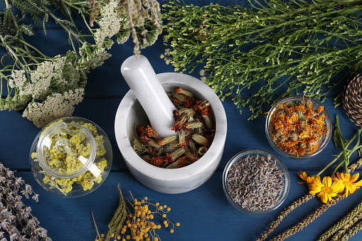 Mortar with pestle and many different herbs on blue wooden table, flat lay