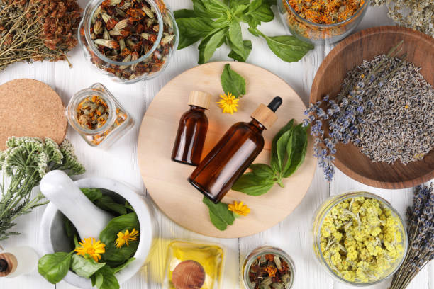istock Bottles of essential oils surrounded by different herbs on white wooden table, flat lay 1935572322