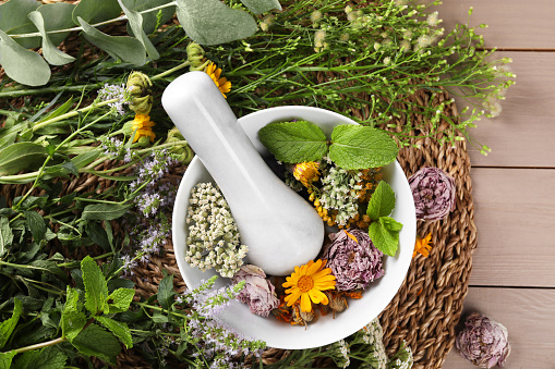 Mortar with pestle and many different herbs on wooden table, flat lay