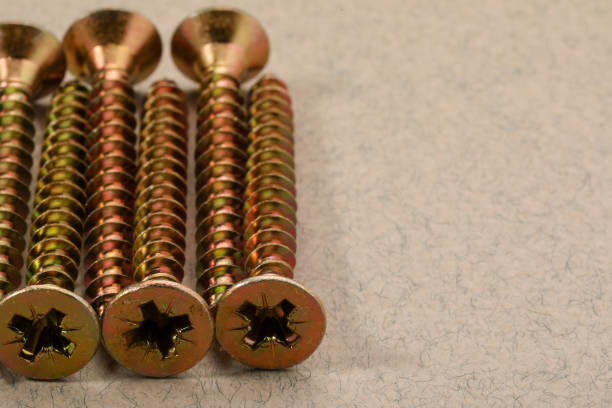 Many metal screws on beige background, closeup. Space for text