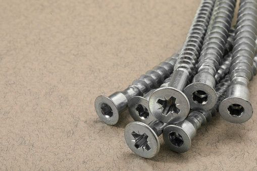 Many metal screws on beige background, closeup. Space for text